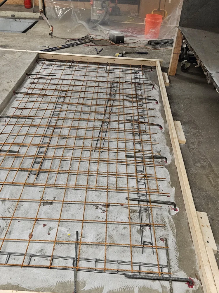 A timber-formed slab with a full mat of reinforcing steel tied out across it and vertical bars standing up through the mat, ready for the pour