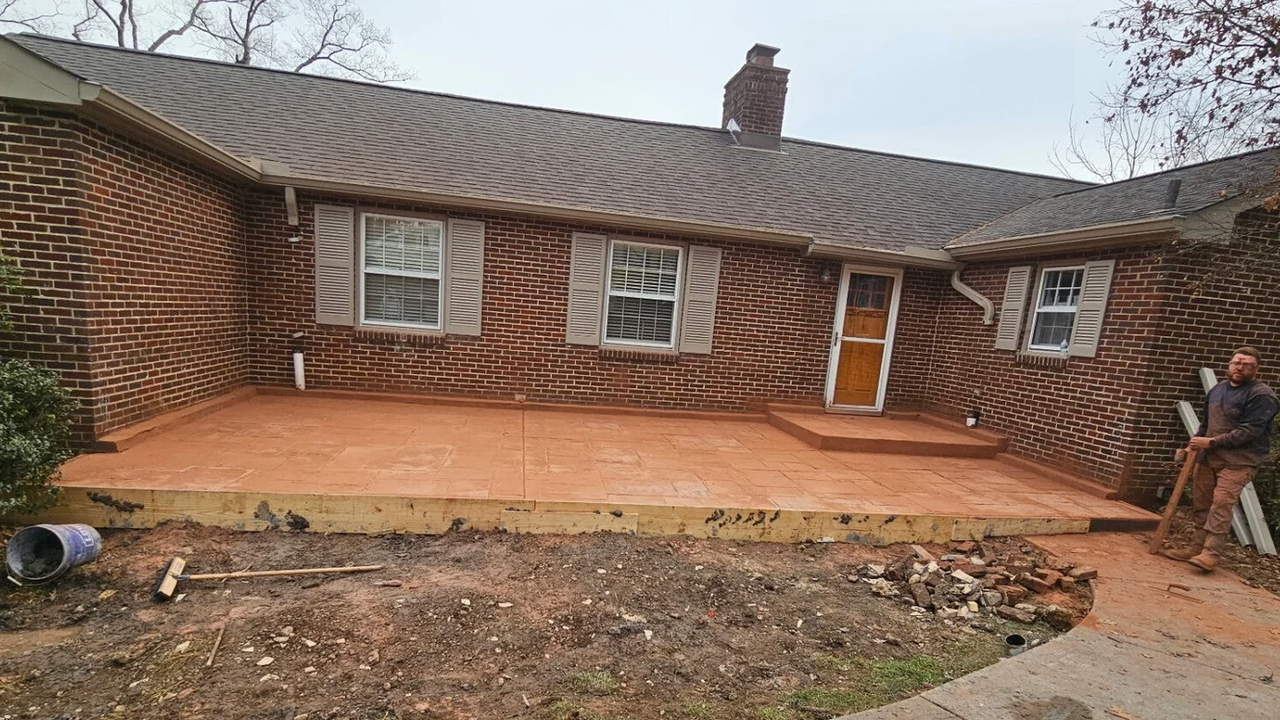 A newly stamped patio behind a red brick house still covered in orange antique release powder, with timber forms along the front edge