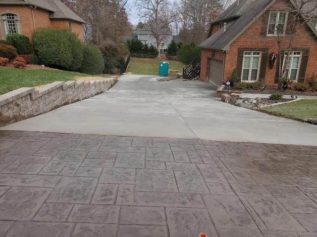 A stamped concrete driveway in a large ashlar pattern running up to a red brick house, meeting a plain gray driveway beyond it with a block wall down one side