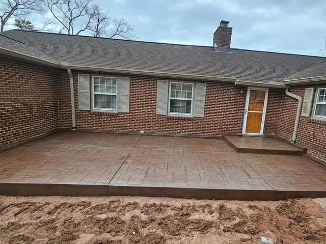 A stamped and colored concrete patio finished along the back of a red brick ranch house, with a raised step up to the back door