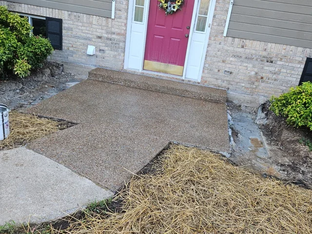 A concrete front walk and landing leading to a pink front door on a brick and gray-sided house, with fresh straw spread over the bare ground either side