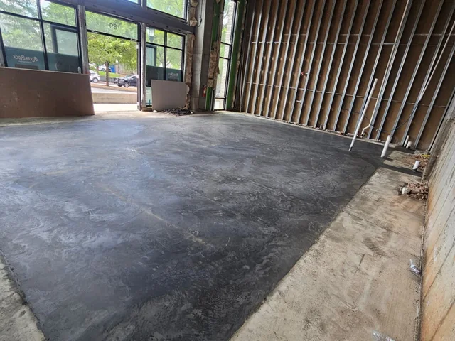 A large interior concrete floor finished smooth and dark inside a commercial space with a glazed wall along one side