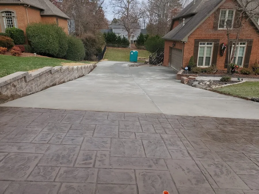 A stamped concrete driveway in a large ashlar pattern running up to a red brick house, meeting the plain gray drive beyond it