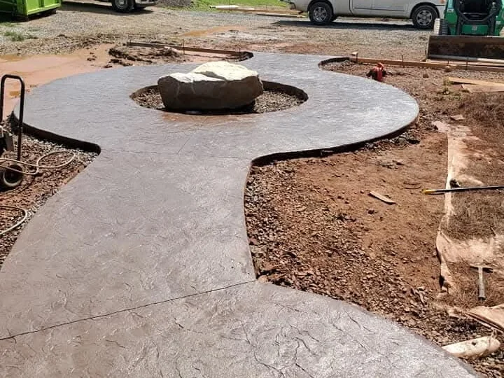 A curved stamped concrete patio laid around a round stone fire pit, with the soil either side not yet made good